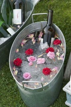 two buckets filled with water and flowers on the grass next to bottles of wine