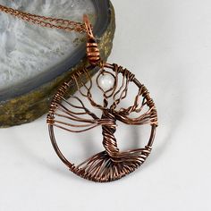 a wire wrapped tree of life pendant sitting on top of a white table next to a rock