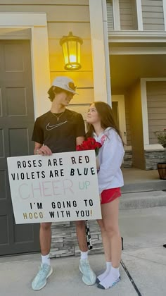 two people standing in front of a house holding a sign that says roses are red violets are blue i'm going to hoco with you