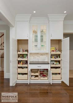 a kitchen with white cupboards and wooden flooring in front of an open pantry