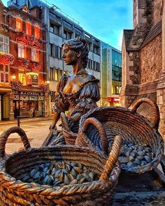 a statue sitting on top of a wooden bench next to baskets filled with shells in front of tall buildings