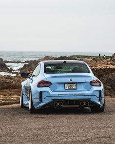 a light blue sports car parked on the side of the road next to the ocean