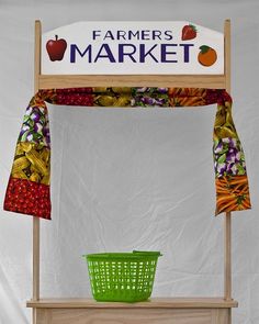 a farmers market stand with a green basket on the top and an apple sign above it