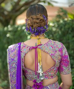 the back of a woman's dress with purple flowers in her hair and jewelry