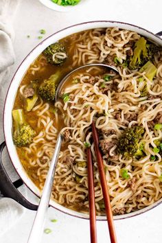 two chopsticks in a bowl of noodles with meat and broccoli on the side