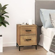 a nightstand with two drawers on top of it next to a bed and a potted plant