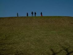 four people standing on top of a hill flying a kite in the sky above them