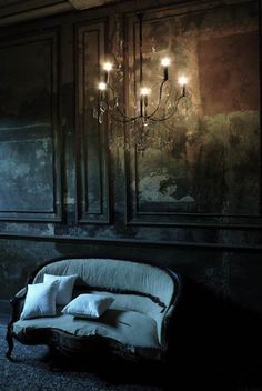 a couch sitting next to a chandelier in a dark room