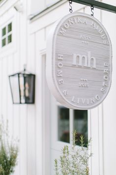 a white sign hanging from the side of a building next to a planter filled with flowers