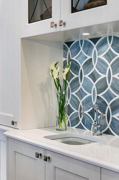 a vase with flowers sitting on top of a kitchen counter next to a sink and cabinets