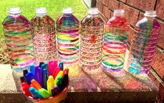 there are many plastic water bottles lined up on the ledge next to each other with colored pencils in them