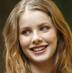 a close up of a person with blonde hair and blue eyes smiling at the camera