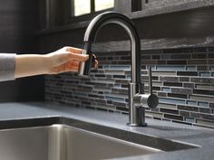 a woman's hand is holding onto the faucet in this kitchen sink