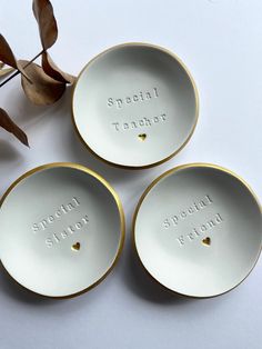 three white bowls with gold rims and words on them