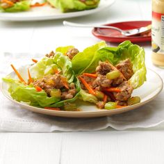 lettuce wraps with meat and carrots on a plate next to dressing bottle