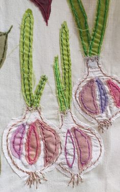 three onions are stitched together on a piece of white fabric with green and red trim