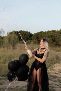 a woman in a black dress is holding some balloons