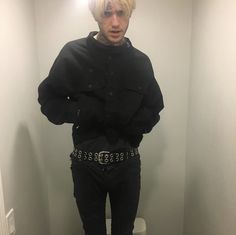 a man with blonde hair standing in front of a mirror wearing black jeans and a jacket