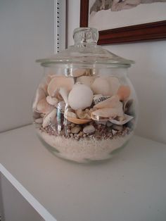 a glass jar filled with sea shells on top of a white shelf next to a mirror