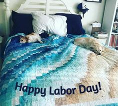 two dogs laying on top of a bed with a happy labor day blanket over it