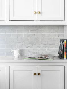 a kitchen with white cabinets and marble backsplash, coffee cup on the counter