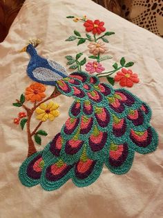 an embroidered peacock sitting on top of a bed