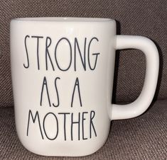 a white coffee mug with the words strong as a mother on it sitting on a couch