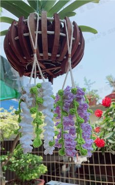 some flowers are hanging from a potted plant in a garden ornament that is decorated with white, purple and green crochet