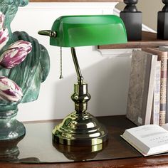 a green lamp sitting on top of a wooden table next to a bookshelf