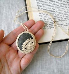 a hand holding a stone with a lace doily on it next to an open book