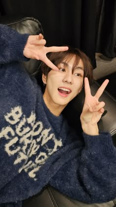 a young man sitting in a chair making the peace sign with his hands while wearing a blue sweater