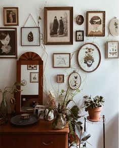 a wall with many framed pictures on it and plants in vases next to the dresser