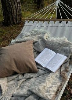 an open book is laying on a hammock in the woods with a pillow