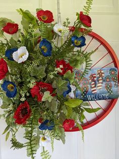 a bouquet of red, white and blue flowers hanging from a door hanger with the welcome sign on it