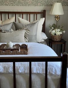 a bed with white sheets and pillows in a bedroom next to a table with flowers