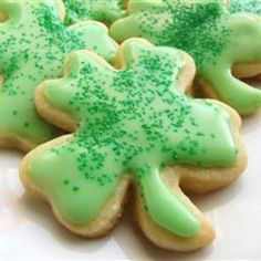 green frosted cookies with sprinkles in the shape of a shamrock on a white plate