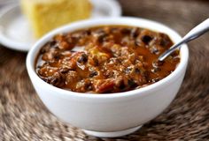 a white bowl filled with chili next to a slice of cake