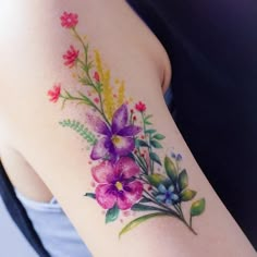 a woman's arm with watercolor flowers and leaves painted on the back of it