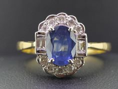 "The simplicity of this ring adds a wonderful statement of elegance. This gorgeous ring would be the perfect Sapphire anniversary ring or 'something blue' for a Vintage bride. Boosting an oval 1.40 carat rich royal blue Ceylon Sapphire secured in a classic four prong setting. Taking center stage amongst half a carat of bright white high premium sparkling Diamonds. The Ceylon Sapphire is flanked by two mille grained set sparkling baguette Diamonds boarded by ten brilliant cut claw set collet edge Classic Blue Halo Ring, Vintage Blue Oval Cluster Ring, Classic Oval Sapphire Wedding Ring, Classic Sapphire Cluster Ring For Wedding, Elegant Blue Oval Cluster Ring, Sapphire Anniversary Ring, Sapphire Anniversary, Gorgeous Ring, Ceylon Sapphire