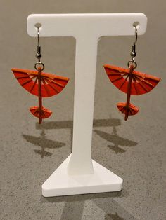 an orange umbrella shaped earrings on a white display stand in front of a gray background