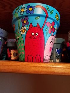 there are many cups on the shelf with cats painted on them and one has a cat in it