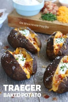 four baked potatoes sitting on top of a wooden table with cheese and other toppings