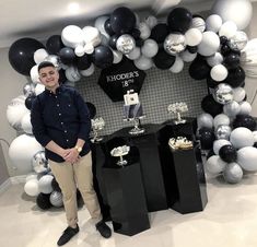 a man standing in front of a table with black and white balloons on it's wall