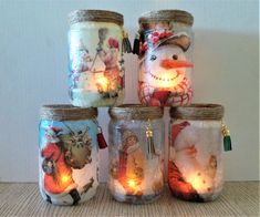 four mason jars decorated with christmas images and lights, one has a snowman on it