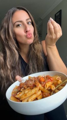 a woman sticking her tongue out while holding a bowl of pasta