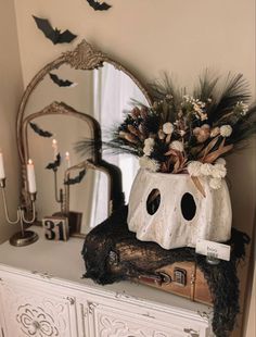 a white dresser topped with a vase filled with flowers and bats next to a mirror