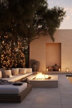 an outdoor fire pit surrounded by lounge chairs and trees with lights on the wall behind it