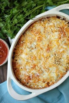 a casserole dish with cheese and parmesan on the side next to some greens