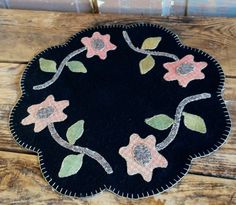 a black round rug with flowers and leaves on the top is sitting on a wooden surface