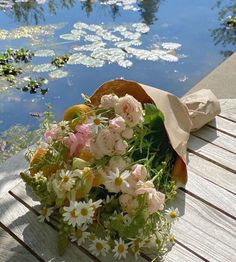 a bouquet of flowers sitting on top of a wooden bench next to a body of water